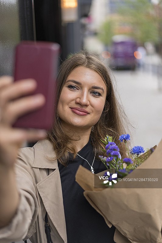 微笑的女子站在人行道上拿着花束自拍图片素材