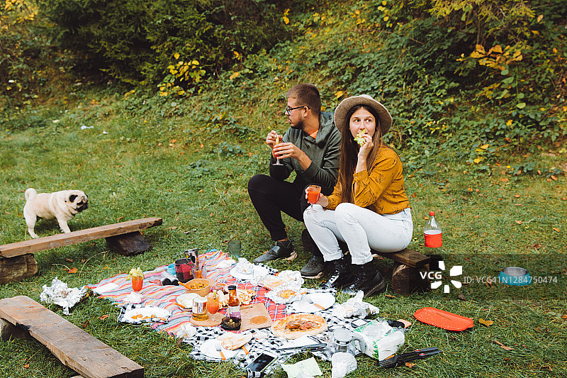 年轻的女人和男人与狗有光明的户外烧烤野餐图片素材