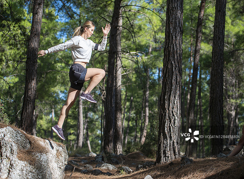 在森林里做运动的女人做着不同的运动。在高山上奔跑跳跃。女子跳高运动员图片素材