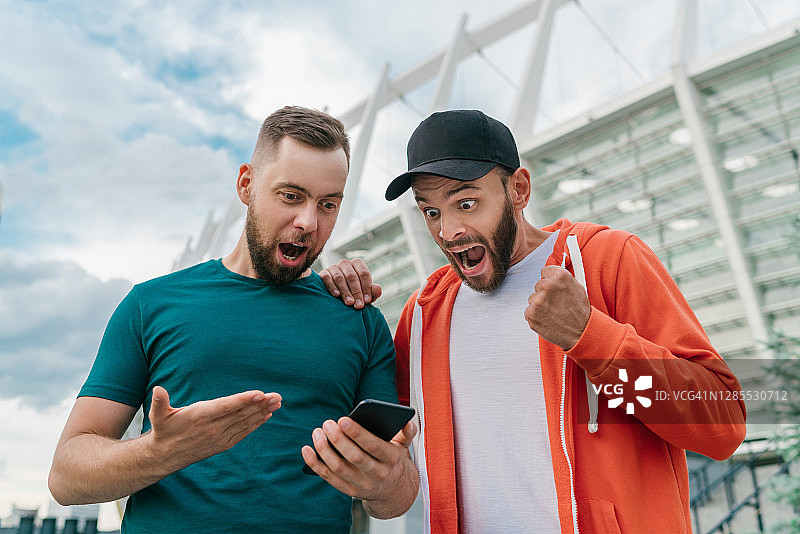两个朋友在以足球场为背景的手机赌博应用中下注后庆祝胜利图片素材