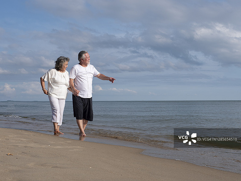 这对浪漫的亚洲老年情侣站在夏日海滩的夕阳下拥抱图片素材