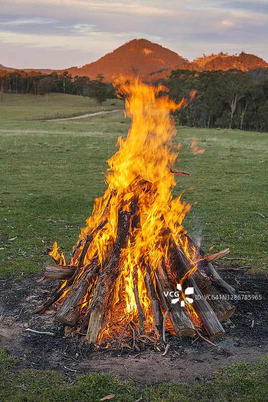 完美燃烧的篝火与山在绿色的田野图片素材