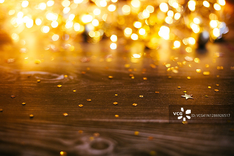 圣诞或新年贺卡。深棕色的木制背景。模糊的仙女灯和金色闪亮的五彩纸屑与复制空间。图片素材