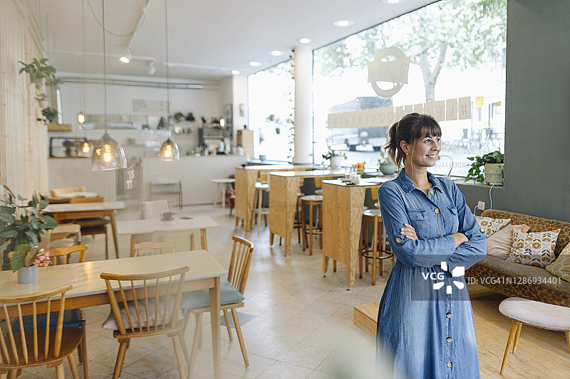 年轻的女企业家双臂交叉，看着别处站在咖啡店图片素材