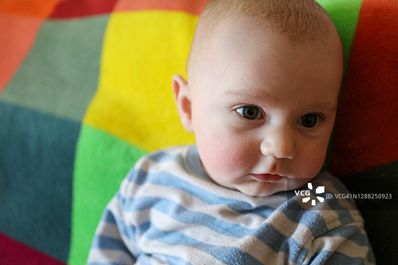 三个月大的男婴在彩色的毯子上四处张望。前视图图片素材