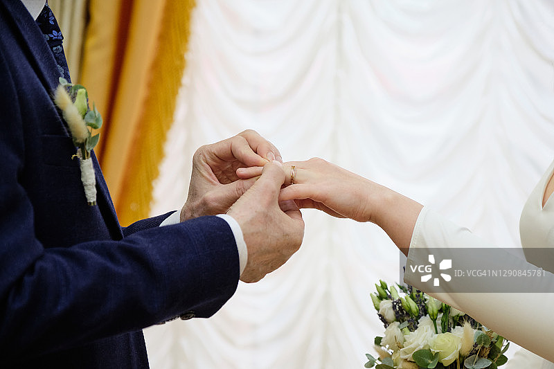 新郎把戒指戴在新娘的手上。婚礼当天新婚夫妇的手，特写。结婚期间交换戒指。图片素材