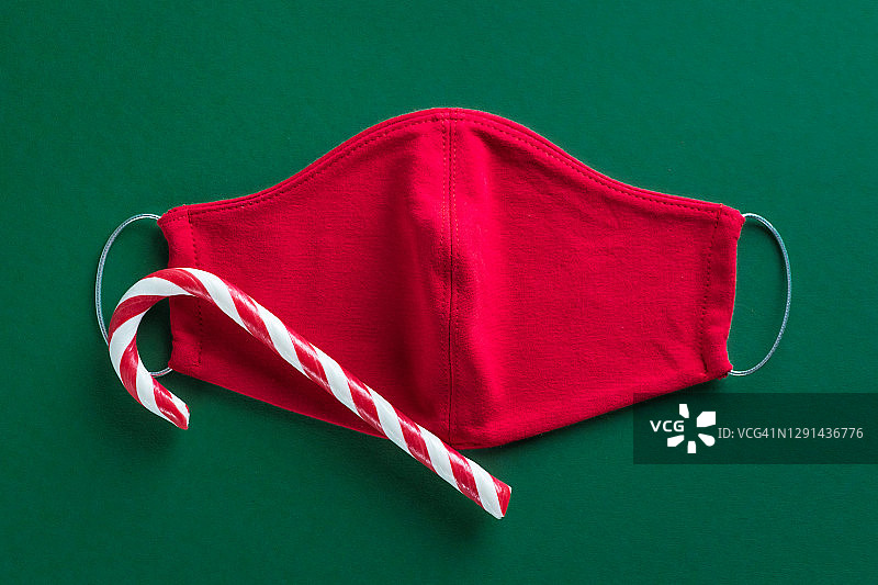 红色医用防护口罩和条纹糖果在绿色的圣诞背景拐杖的形式。预防和预防COVID - 19大流行的传播。一个快乐健康的圣诞节的概念。图片素材