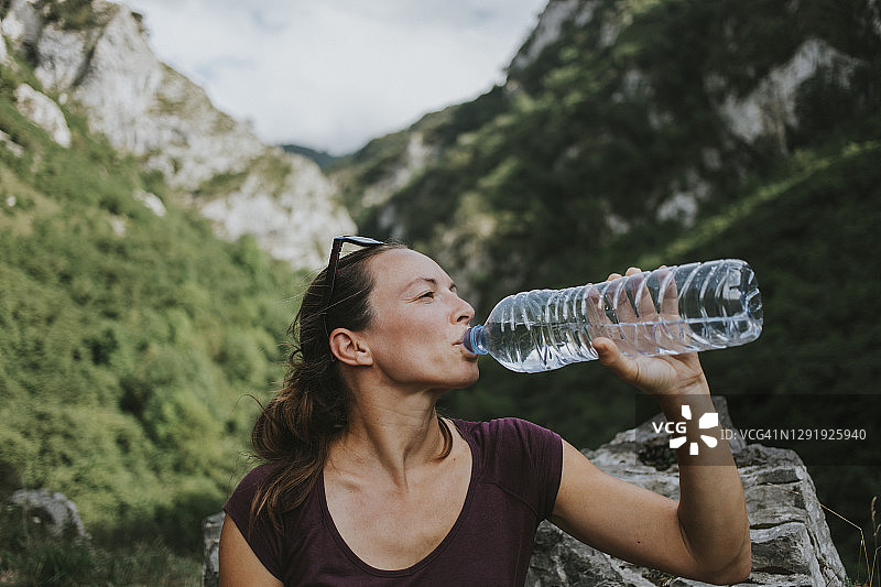 中年女性徒步旅行者一边喝着塑料水瓶，一边看向别处图片素材