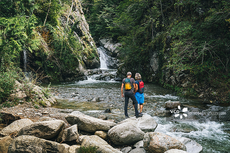 清晨，一对成熟的徒步夫妇在瀑布旁放松图片素材
