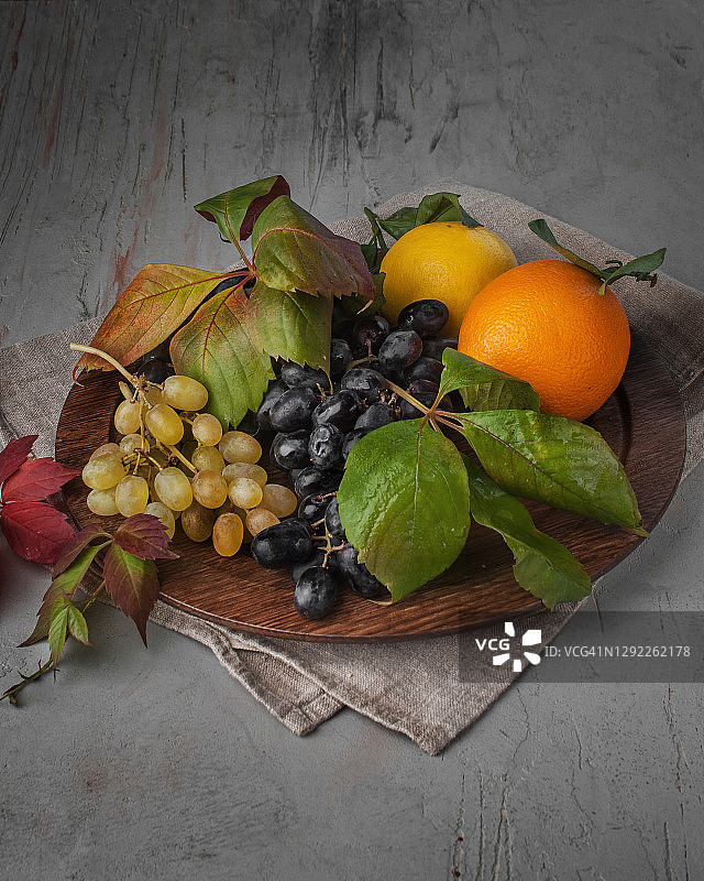 食物摄影木盘与新鲜水果，葡萄和橙子与叶片侧视图上的灰色纹理背景近景图片素材