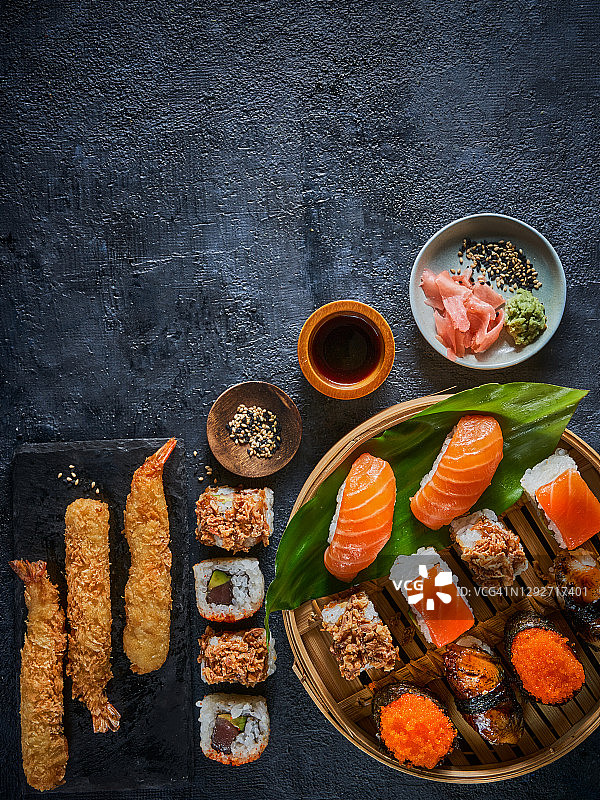 平铺的日式料理——寿司、手握寿司、天妇罗、寿司、生鱼片，深色的背景上有复制空间。传统的日本料理。亚洲餐厅概念菜单。图片素材