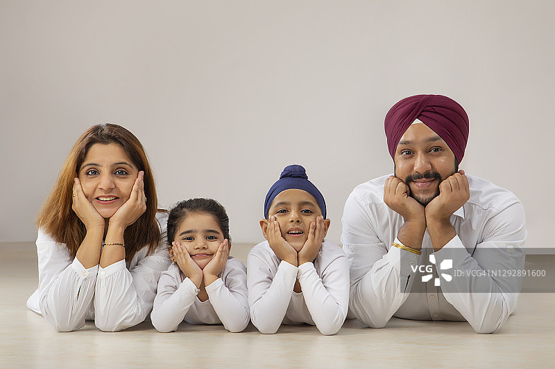 一个快乐的锡克教家庭微笑着，双手托着下巴一起在地板上摆姿势图片素材