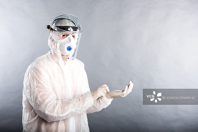 一名穿着防护个人防护服的医生演示了如何使用它来抗击冠状病毒COVID-19病毒。照片在灰色背景在工作室图片素材