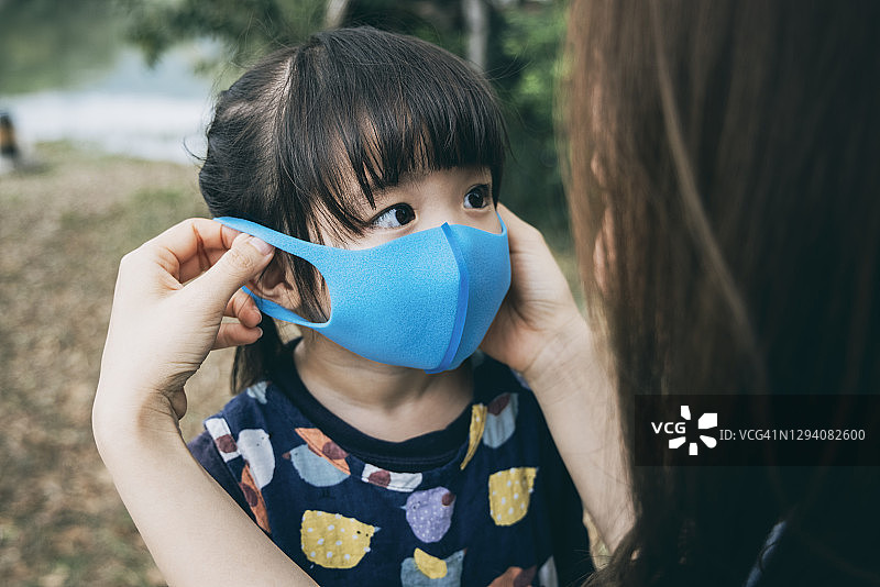 母亲在公园为小女儿戴上外科口罩，防止感冒、流感和病毒的传播图片素材
