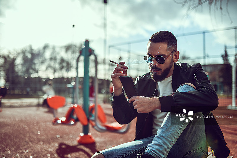 男性在健身公园吸烟和使用智能手机图片素材