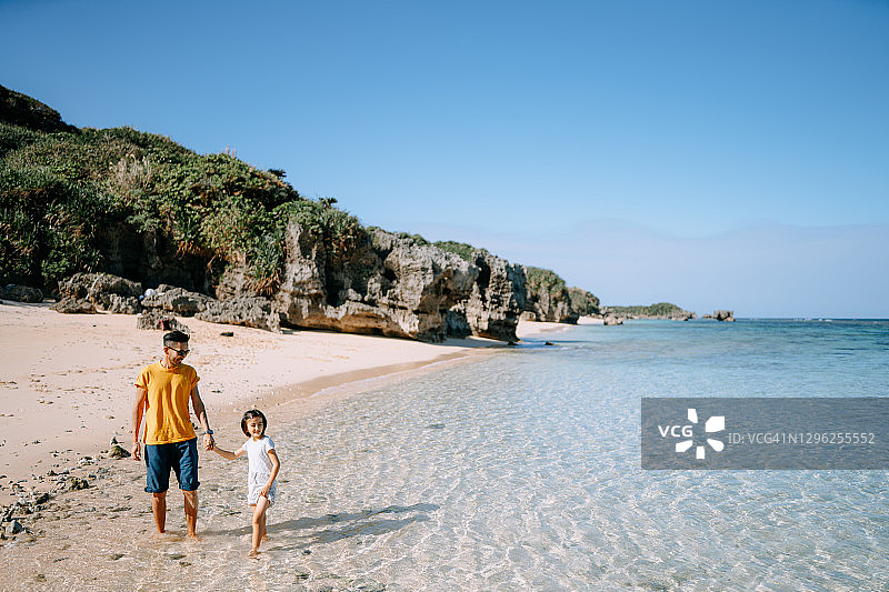 父亲和年幼的女儿走在热带海滩，日本图片素材
