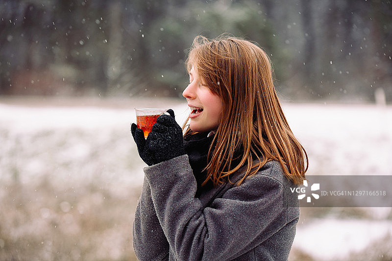 冰冻但满足可爱的金发女孩与一杯热茶的背景霜冻的冬季森林景观图片素材