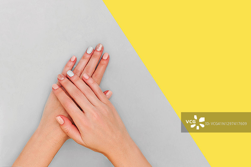 女人的手与柔和的指甲在灰色和黄色的背景。颜色2021。图片素材