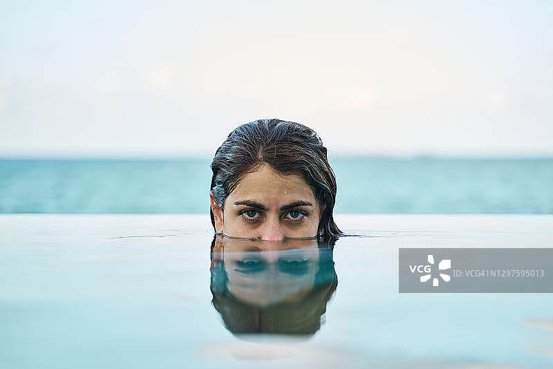 平静的年轻民族妇女把半张脸伸出游泳池的水在海边图片素材