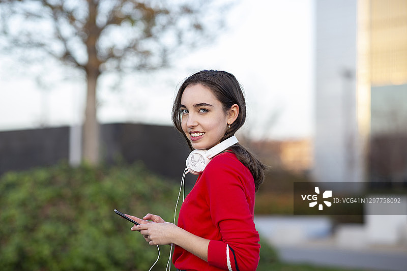 年轻女子戴着耳机和智能手机在公园里图片素材