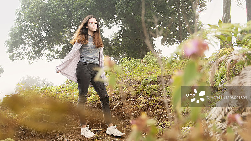 年轻女子站在有树叶和雾的山路上图片素材