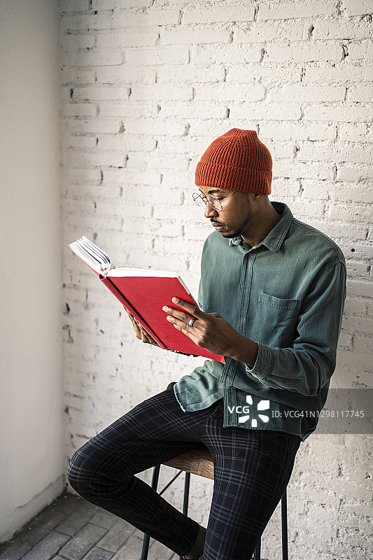 一个戴眼镜的男人靠着白砖墙看书图片素材