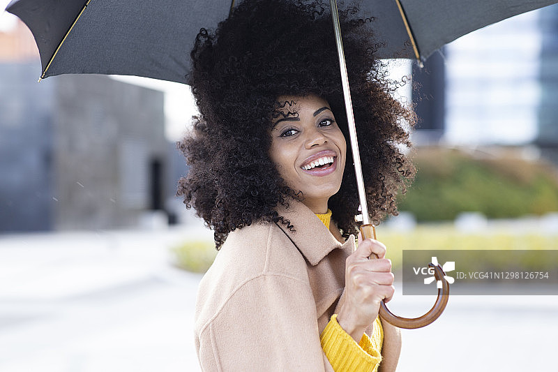 微笑的女人穿着夹克拿着雨伞站在户外图片素材