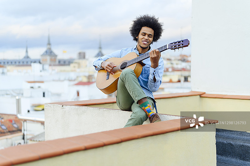 一个留着卷发的年轻人坐在阳台上弹原声吉他图片素材