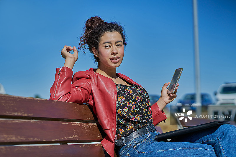 在户外打电话的女人。这是一幅年轻的商业女性坐在户外长椅上打电话的肖像。经营理念。图片素材