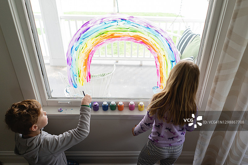 兄弟姐妹在客厅窗户上画彩虹图片素材