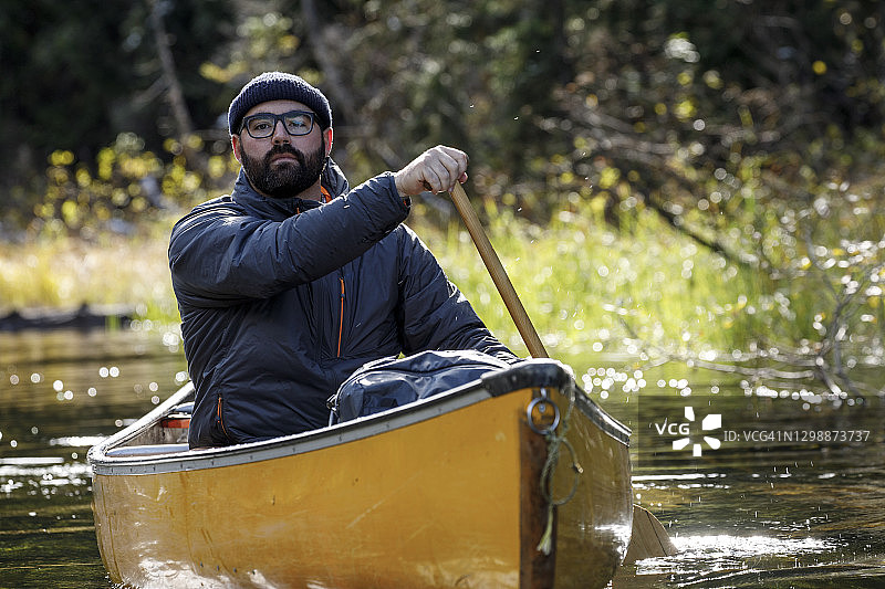 一位戴着帽子和眼镜、满脸胡须的真诚男子在平静的湖面上划着独木舟图片素材