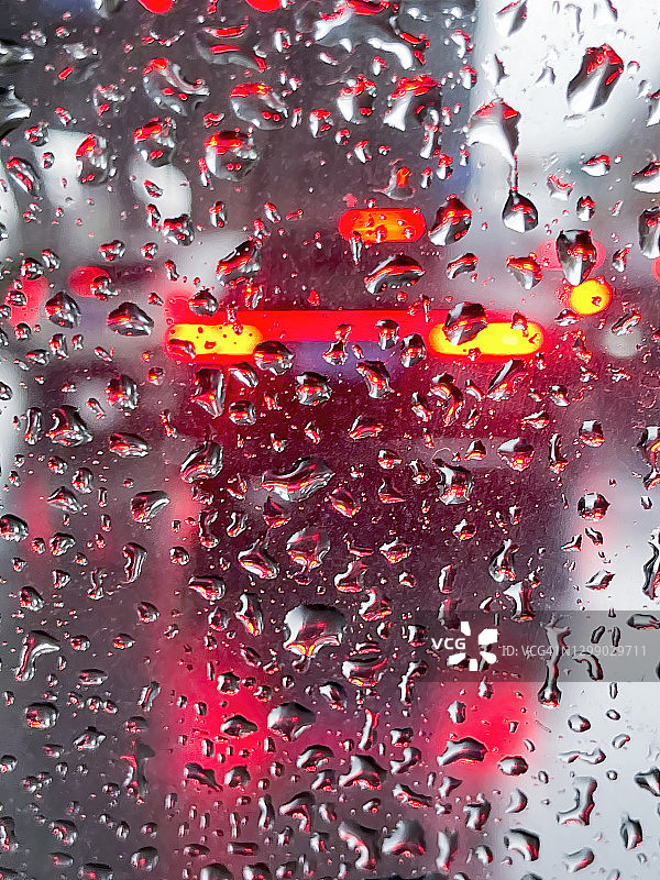 在一个下雨天，被水滴覆盖的玻璃模糊了汽车前面的尾灯图片素材