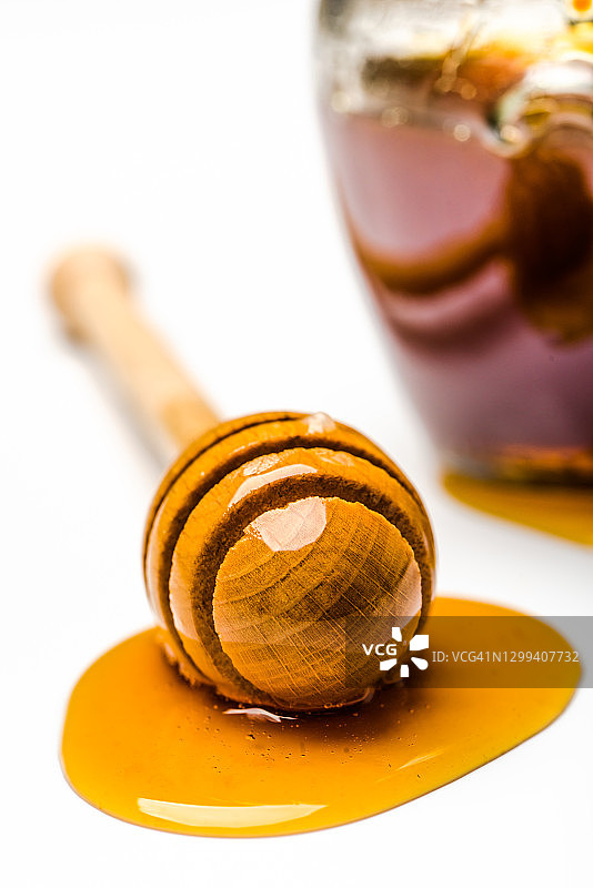 蜂蜜滴，勺子和白色背景下的蜂蜜玻璃罐图片素材