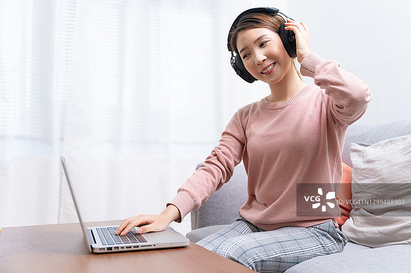 一个亚洲女人在客厅用笔记本电脑听音乐图片素材