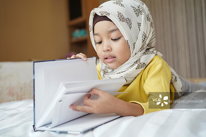 快乐的亚洲穆斯林女孩在家里读这本书。图片素材