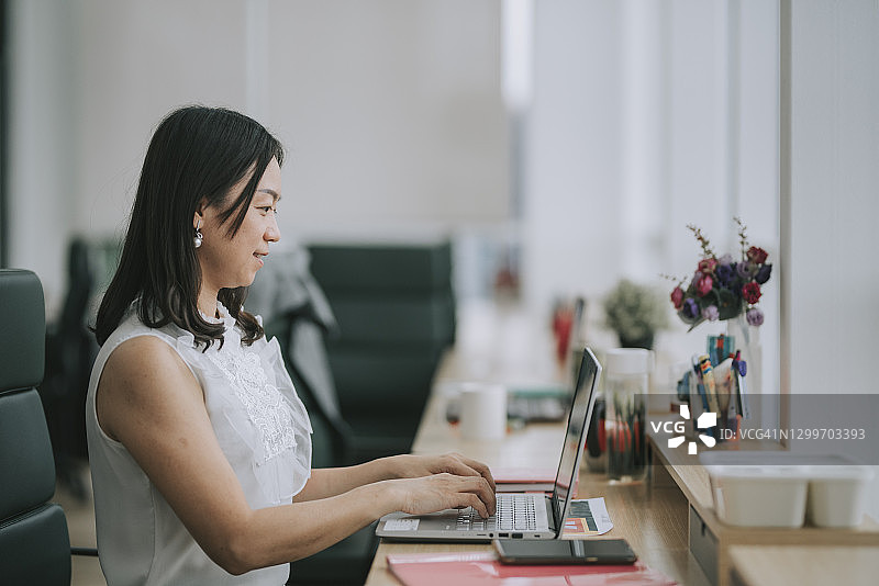 亚洲华裔女白领，在办公室用笔记本电脑打字图片素材