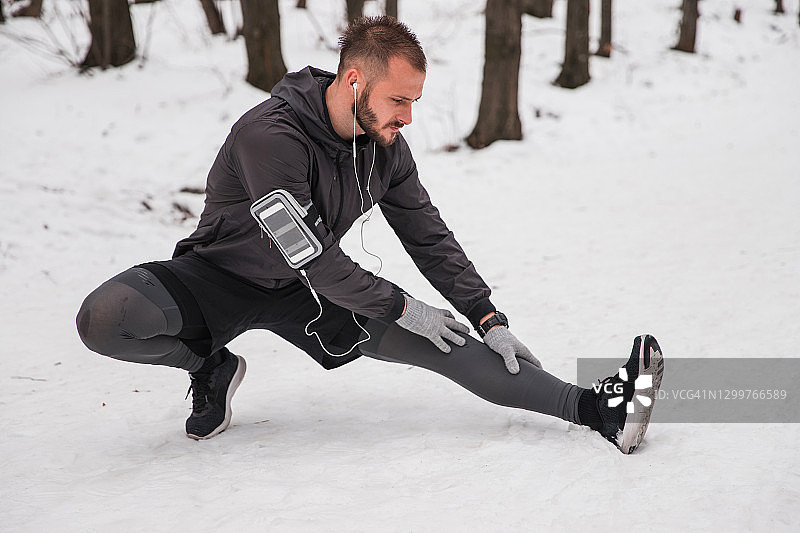 健康人在雪地上用手机和耳机做腿部运动图片素材
