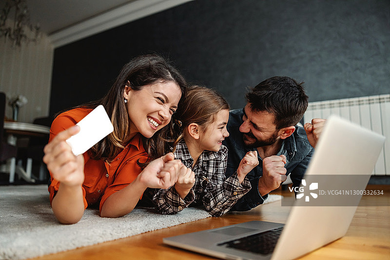 快乐的家庭使用笔记本电脑进行网上购物。他们对购买感到兴奋。妈妈拿着信用卡。图片素材
