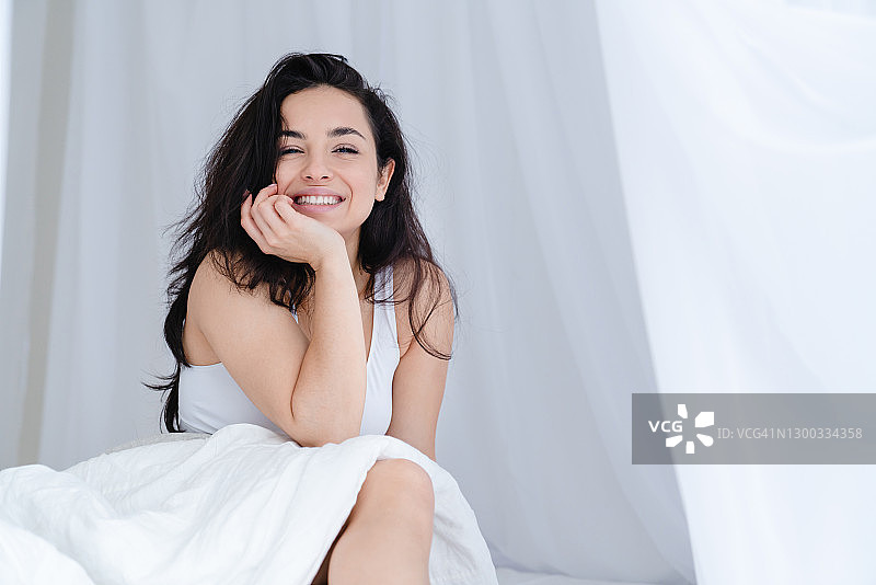 微笑的年轻白人女子在床上放松在卧室的早晨图片素材