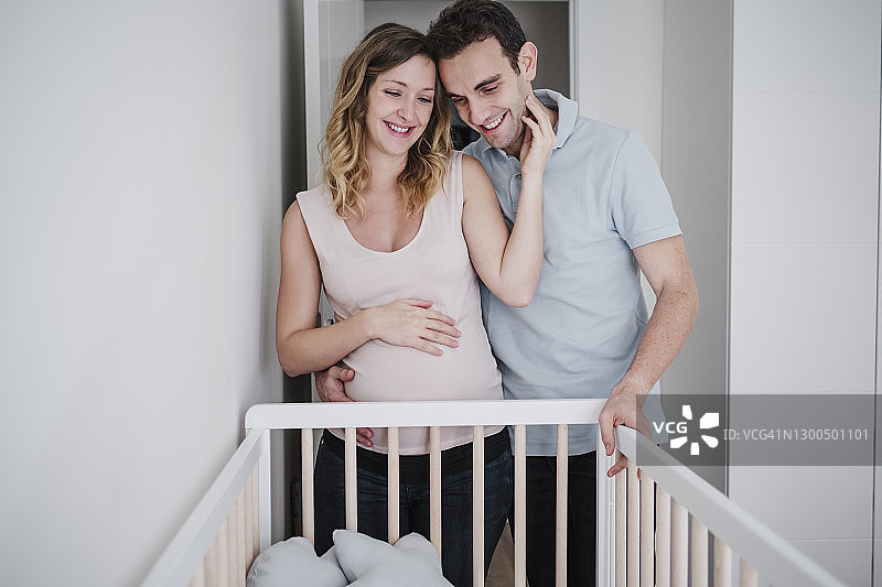 幸福怀孕的妻子和丈夫站在家里的婴儿床旁图片素材