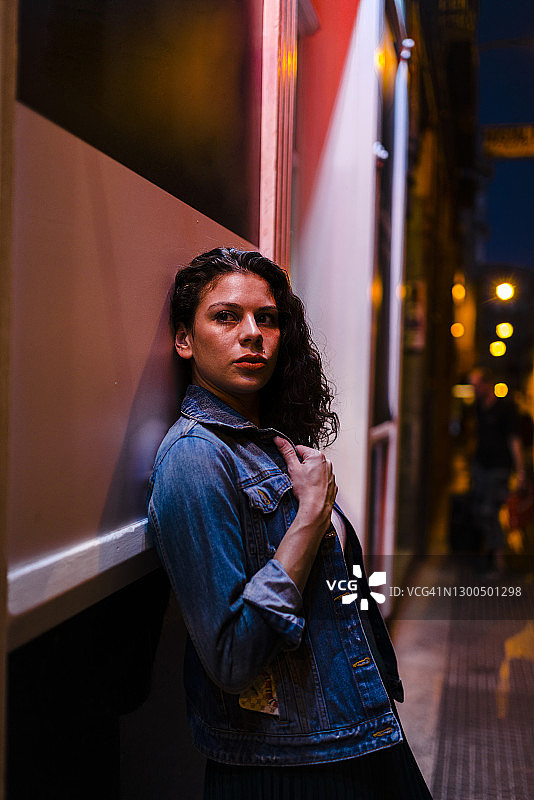 在城市的夜晚，一个沉思的年轻女子靠在墙上图片素材