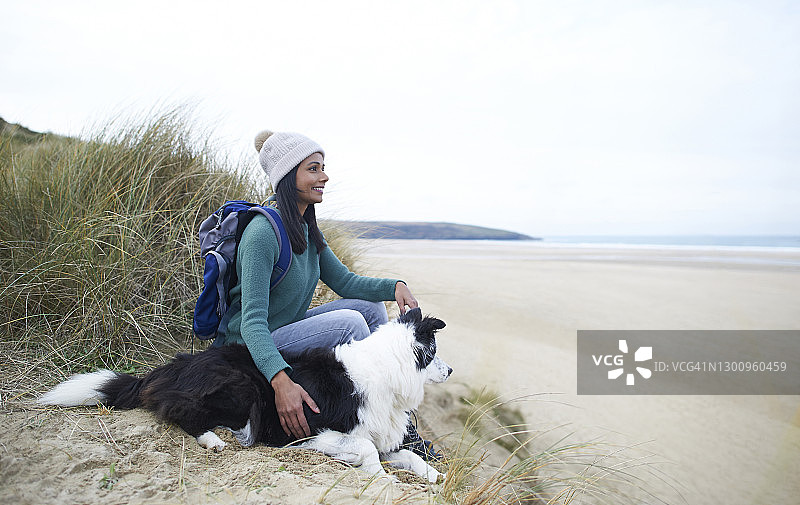 快乐的徒步旅行者和狗一起坐在海滩上。图片素材