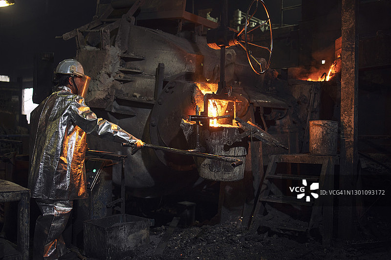 铸造工人将热钢倒入桶中进行金属铸造。铁的生产和熔化。图片素材
