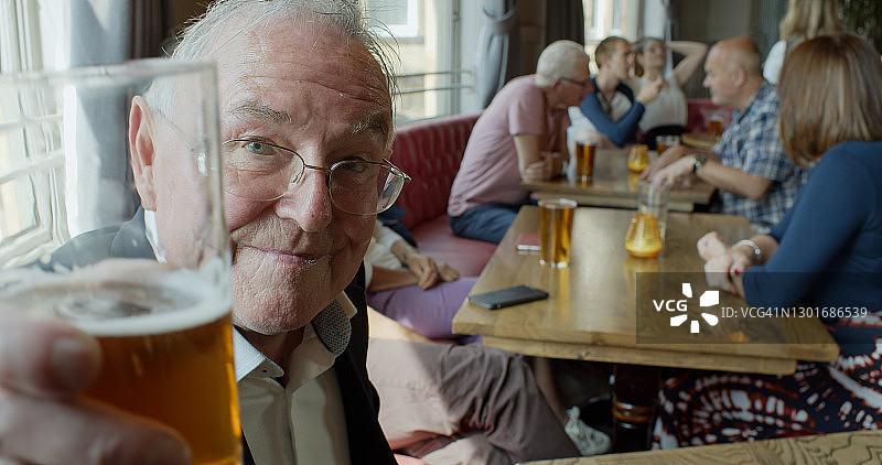 老男人在拥挤的酒吧向镜头举起啤酒图片素材