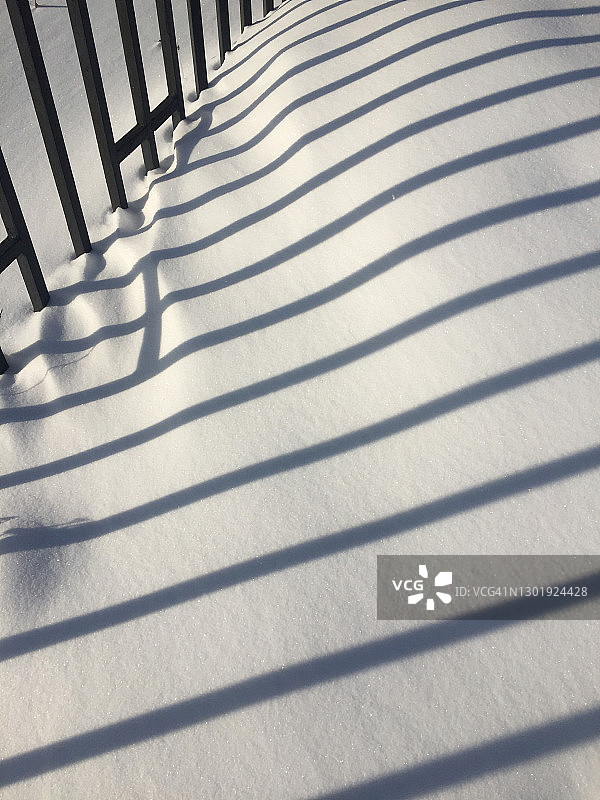 栅栏和栅栏的影子在阳光明媚的日子雪地上。白色上的对角线平行线图片素材