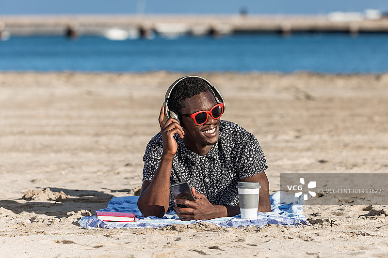 快乐的黑人戴着智能手机和耳机在海滩上享受图片素材