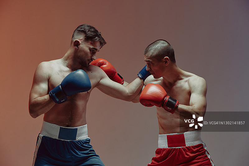 拳师格斗的两名格斗男性戴着拳击手套在红棚轻拍，武术、混合格斗的概念图片素材