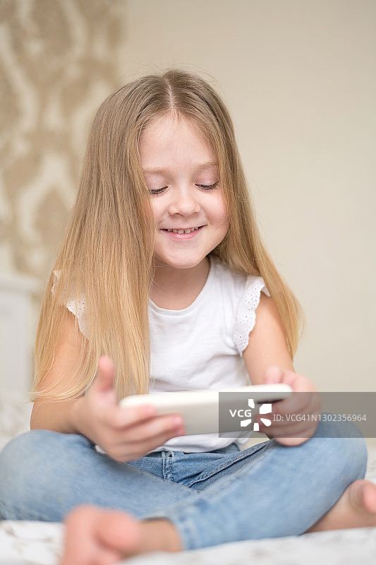 一个小女孩躺在床上玩手机社交网络。图片素材