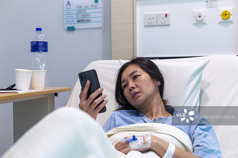 女病人在医院病床上用智能手机看书图片素材