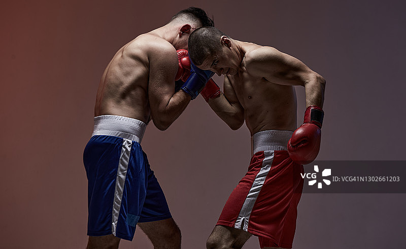 拳师之战中，两名男性拳手戴着拳击手套在红棚轻拍，武术、混合格斗概念图片素材
